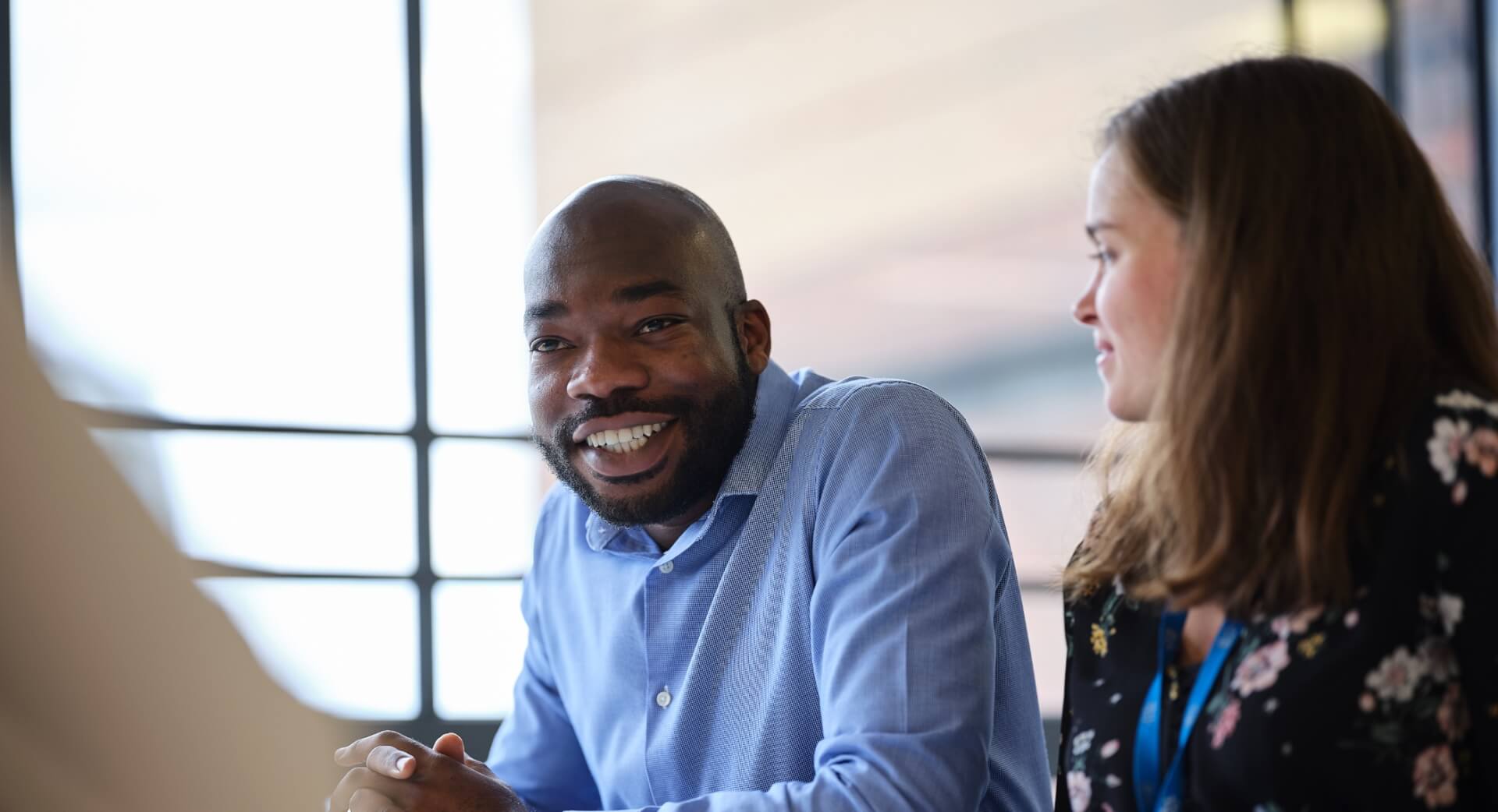 A man and woman engaged in a group conversation. The man is talking whilst the woman looks at him 