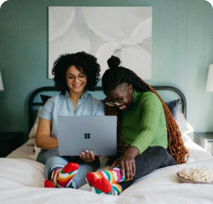 women sitting on a bed using a laptop