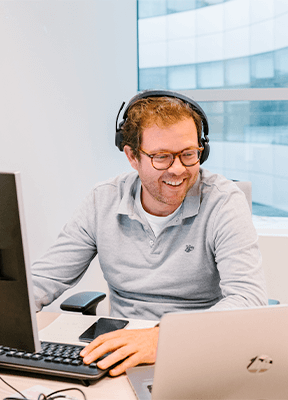 A smiling man sitting at his workstation wearing a headset 