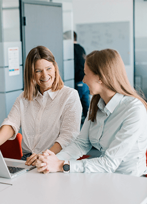 two young women laughing and chatting in front of their computer