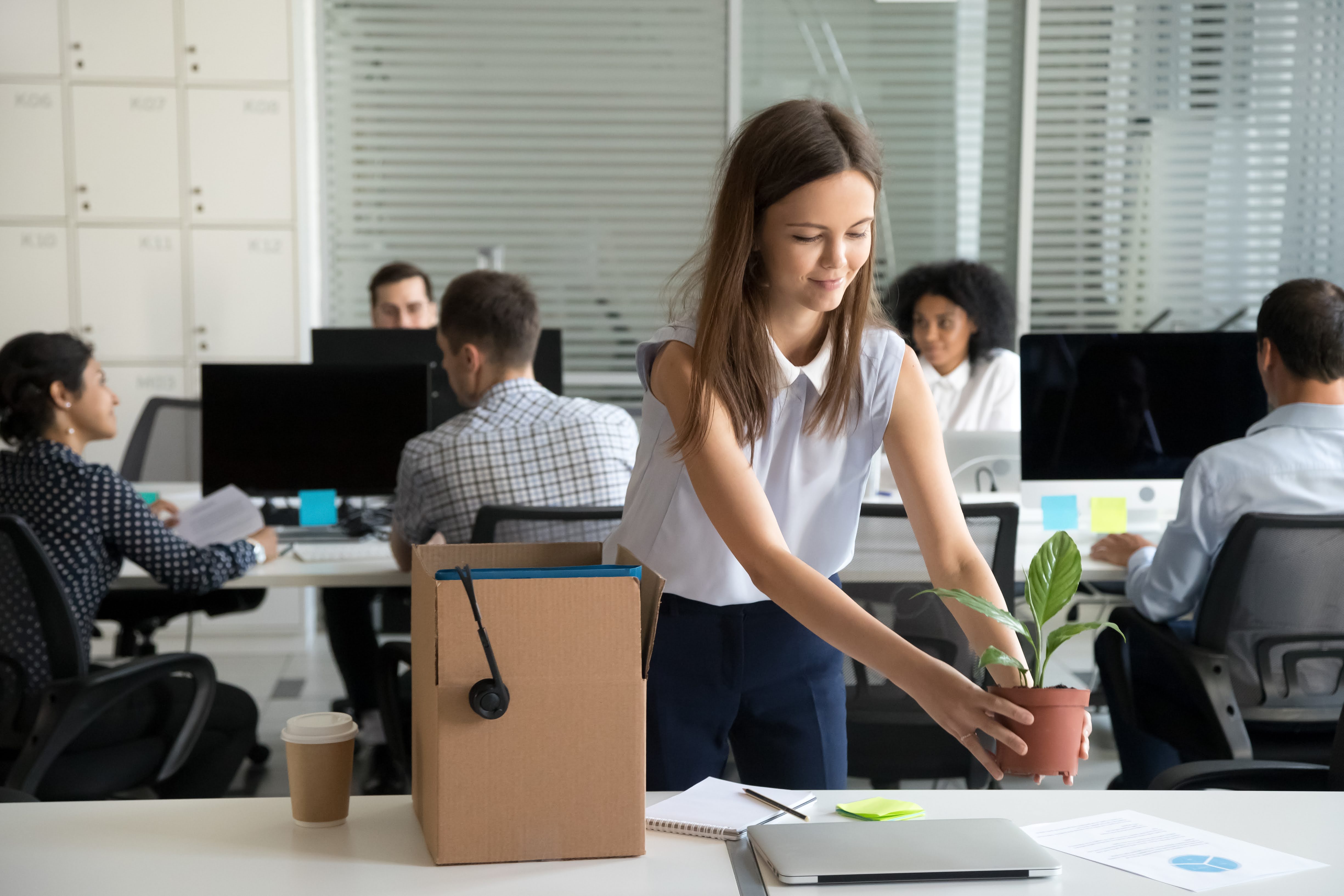 Woman placing a plant on her desk with a group of employees behind her