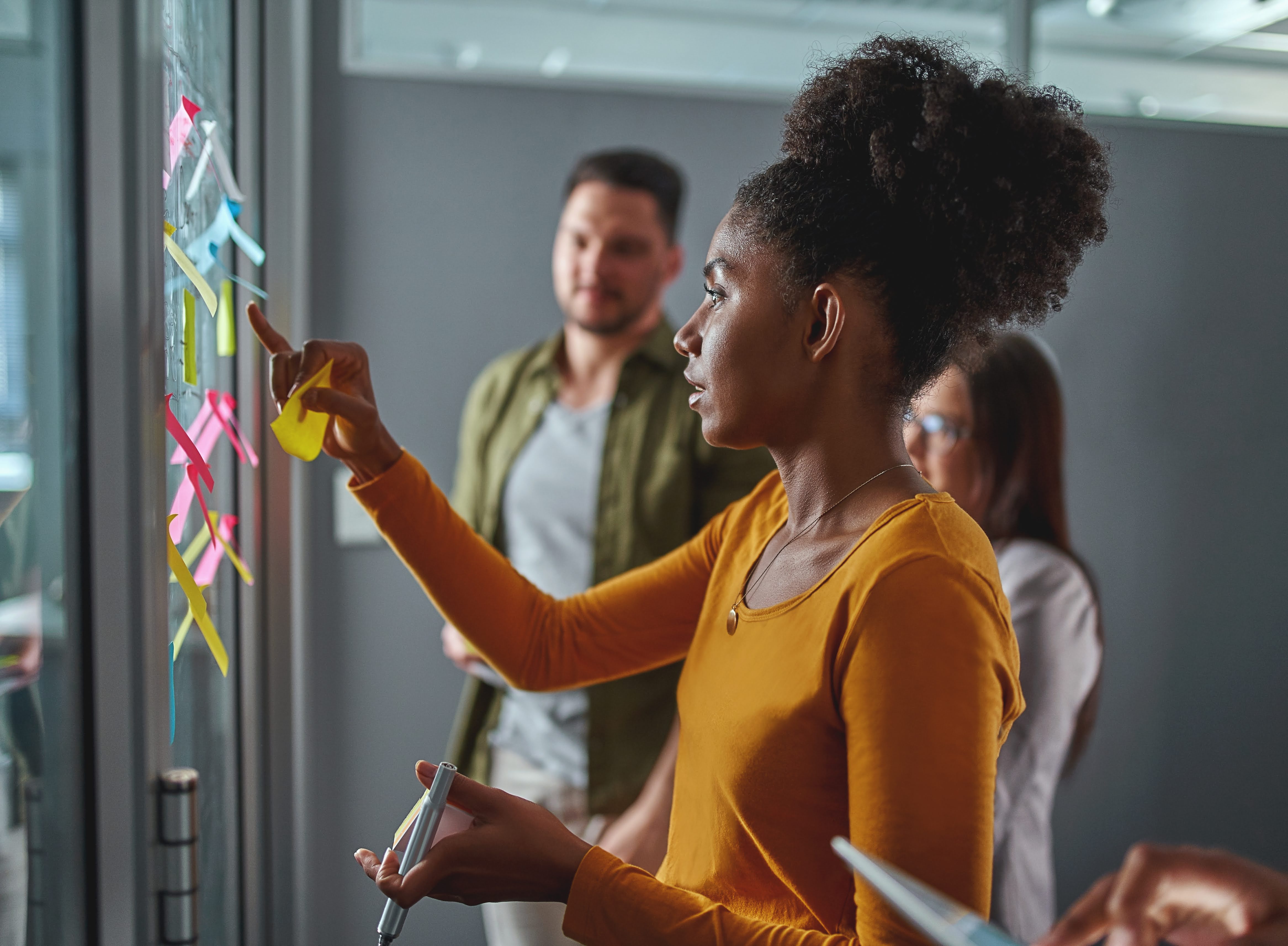 A woman sticking posting sticky notes on a window with her colleagues behind 