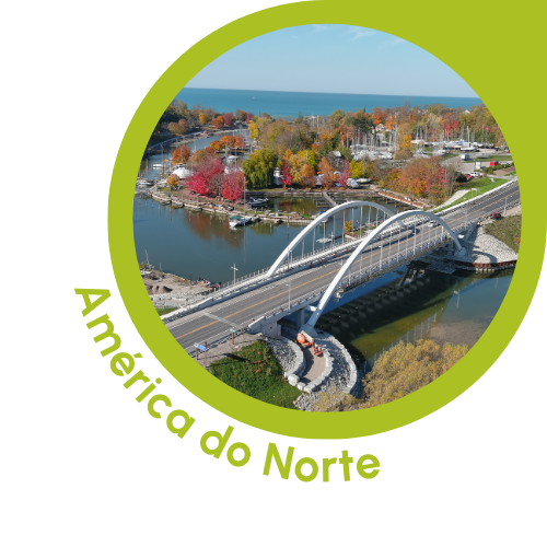 Uma imagem circular com uma borda verde que mostra uma vista panorâmica da América do Norte. A imagem apresenta uma ponte sobre um rio, cercada por folhagens de outono em tons vibrantes de vermelho, laranja e amarelo. No plano de fundo, há barcos atracados em uma marina e um corpo de água que se estende até o horizonte. O texto “América do Norte” está escrito em verde, curvando-se ao longo da borda inferior esquerda do círculo, indicando o contexto norte-americano da cena.