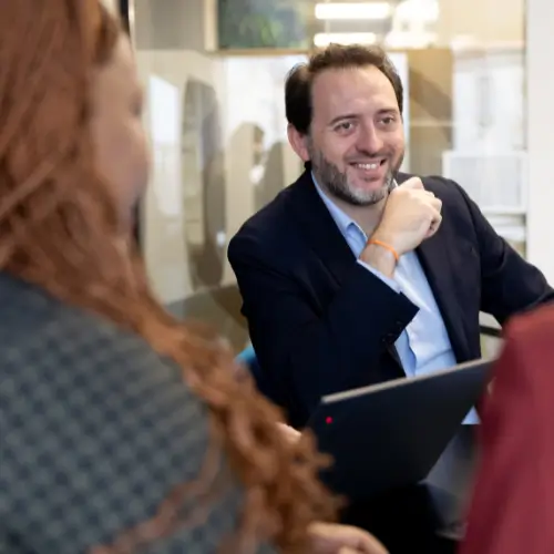 Une réunion professionnelle dans un bureau moderne, avec des personnes engagées dans une discussion et une collaboration, centrée sur une personne en costume utilisant un ordinateur portable.