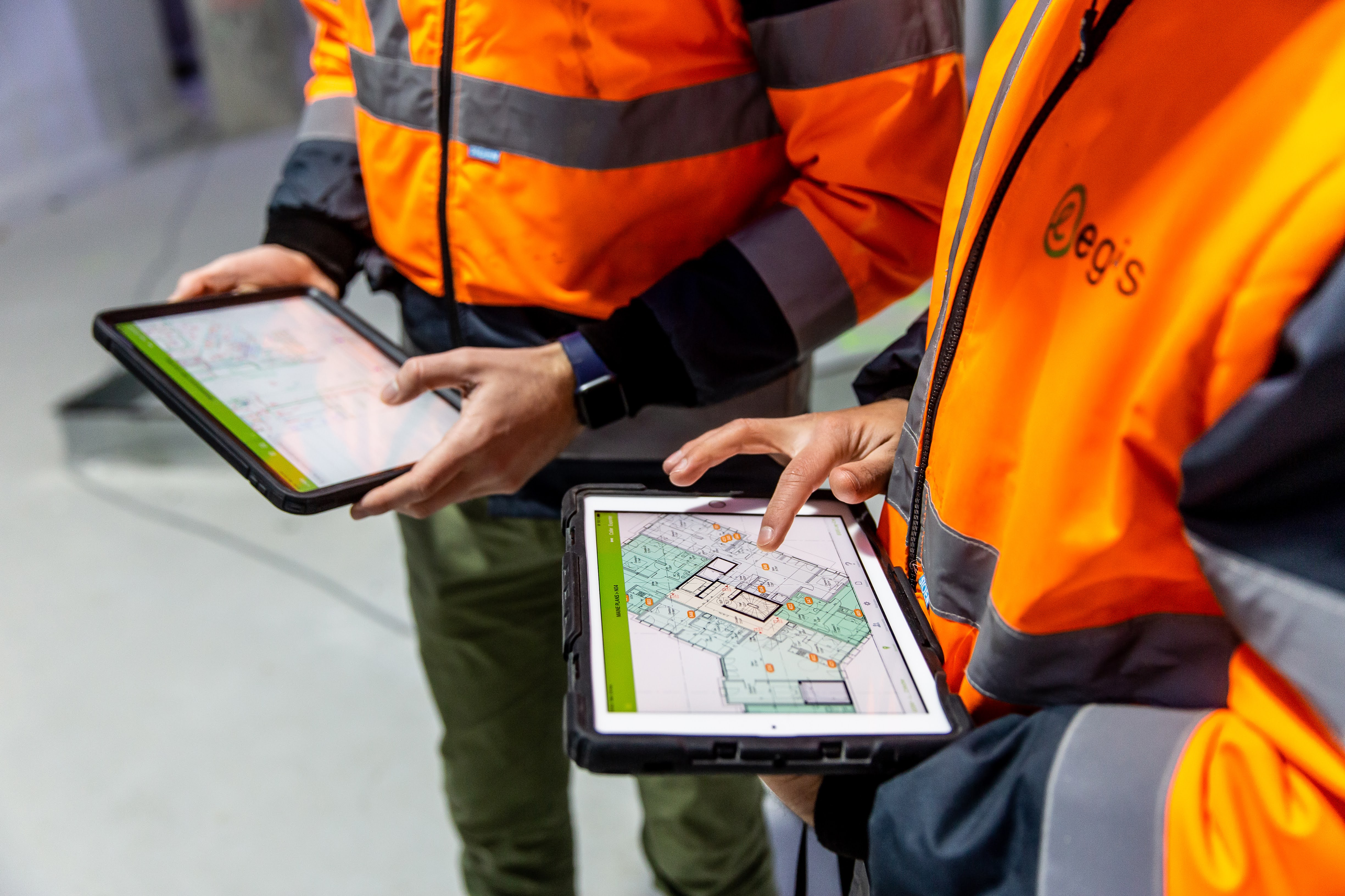 Two people in high vis jackets looking at floor plans on digital tablets