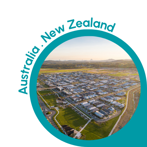 A circular image with a teal border showing a panoramic view of a suburban area in Australia or New Zealand. The image features a well-organised residential neighbourhood with rows of houses, green lawns and winding streets. The background includes open fields and distant hills under a clear sky. The text ‘Australia . New Zealand’ is written in teal, curving along the top left edge of the circle, indicating the context of Australia and New Zealand.