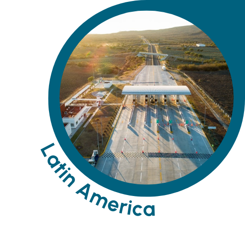 A circular image with a teal border showing a toll plaza on a motorway in Latin America. The image features several lanes of the motorway passing the toll booths, with the surrounding infrastructure and open land stretching into the distance. The scene is bathed in warm sunlight, suggesting early morning or late afternoon. The text ‘Latin America’ is written in teal, curving along the bottom left edge of the circle, indicating the Latin American context of the scene.