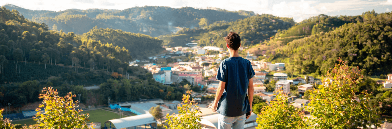 一个男孩看着满是自然、房屋和多云天气的风景。