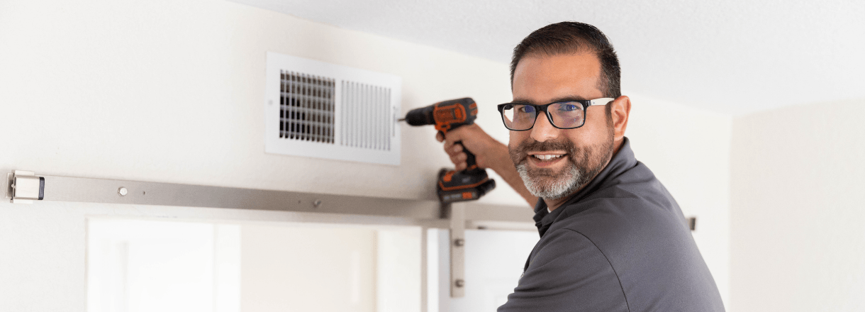Maintenance tech fixing a grill to the wall
