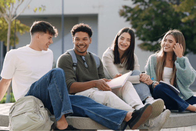 Four students sitting outdoors together, reviewing notes and studying on a university campus.