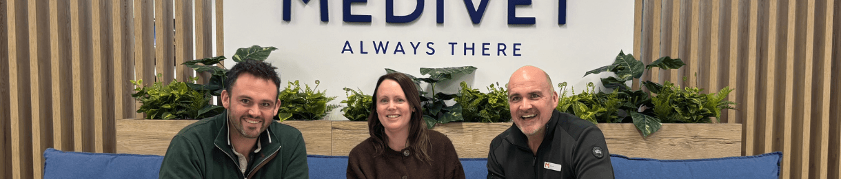 Medivet team sat smiling in front of a Medivet sign