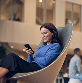 A woman with brown hair, looking at her phone smiling