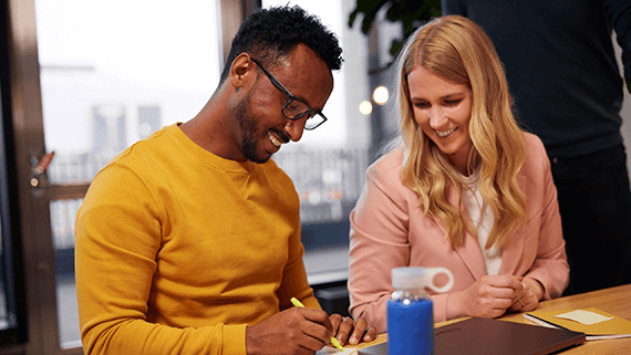 Two colleagues writing on a post-it note while smiling