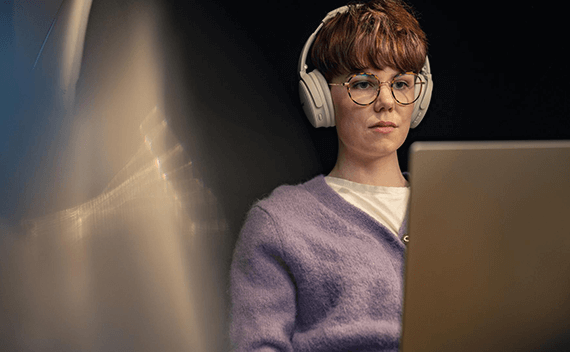 A woman sitting by her computer with headphones on