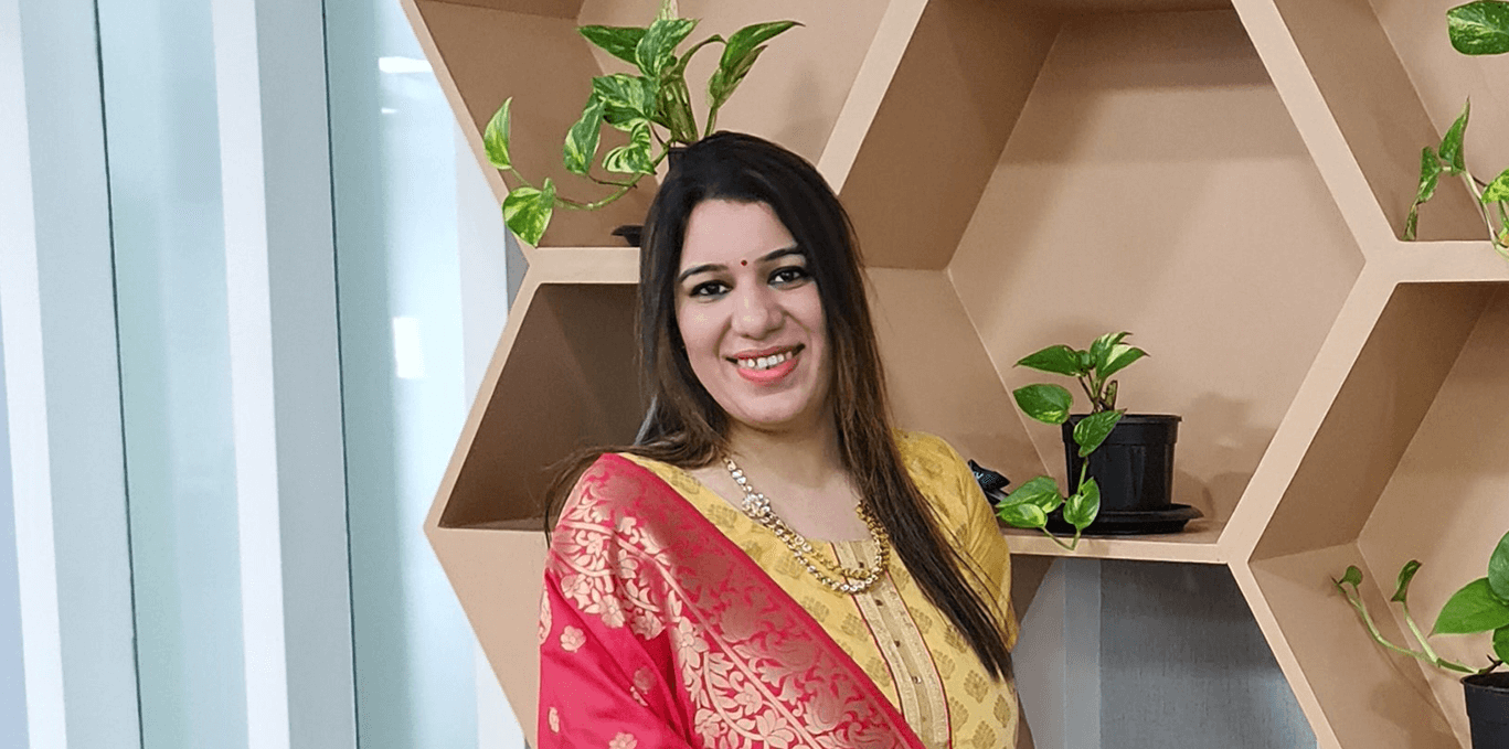 Priyanka standing in front of a shelf and smiling.