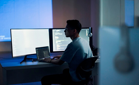 A man sitting in front of three screen working on some code.