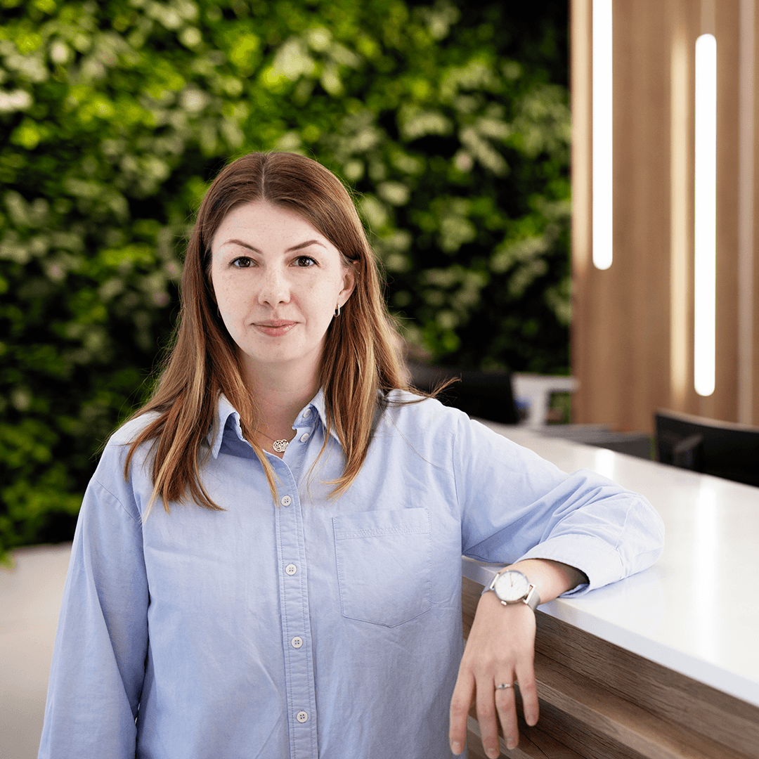A woman with brown hair standing by a reception and looking into the camera