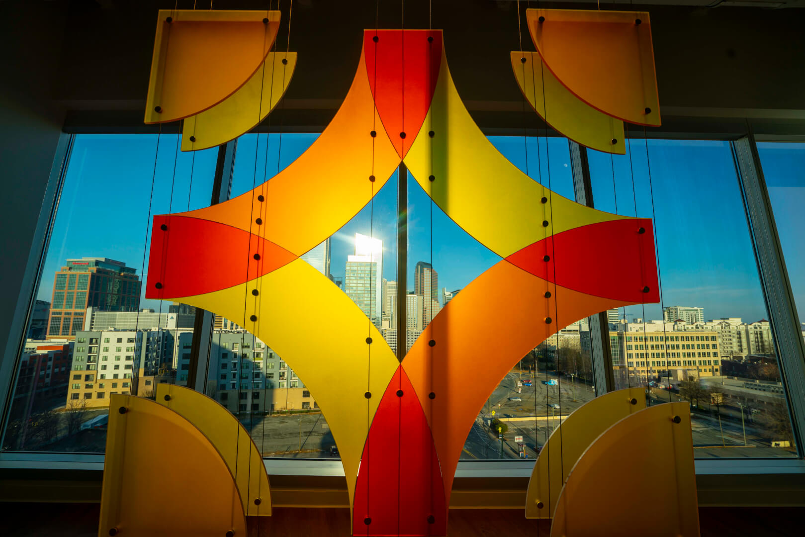 Colorful geometric hanging art in front of a city window view.