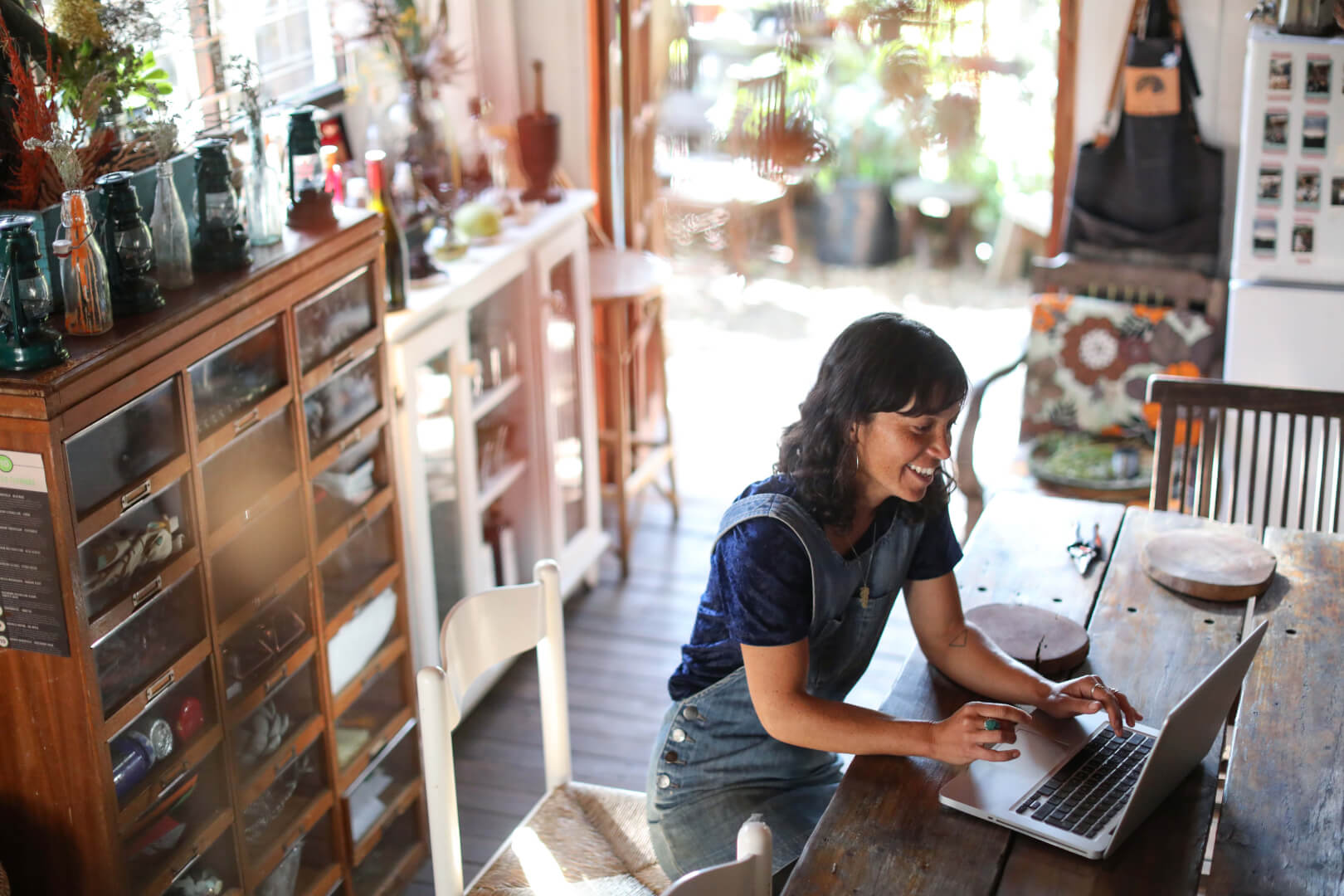 Smiling woman using a laptop at home in a cozy, rustic kitchen.