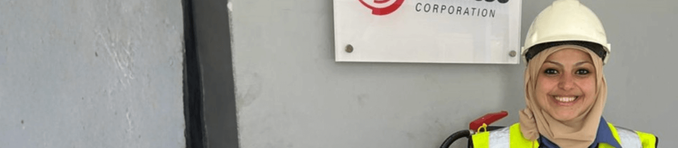 Shereen standing next to a wall with a Wabtec sign wearing a hard hat