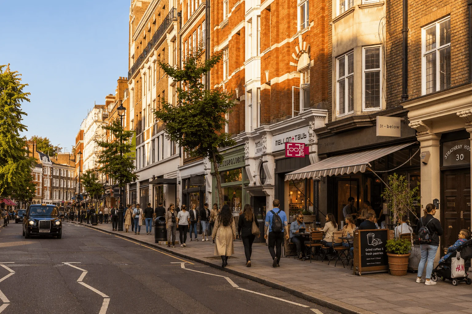 Street view in Marylebone with red-brick buildings, independent shops and cafés, and people walking along a busy pavement.